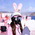 Person wearing a pink bunny helmet with rabbit ears on a snowy background